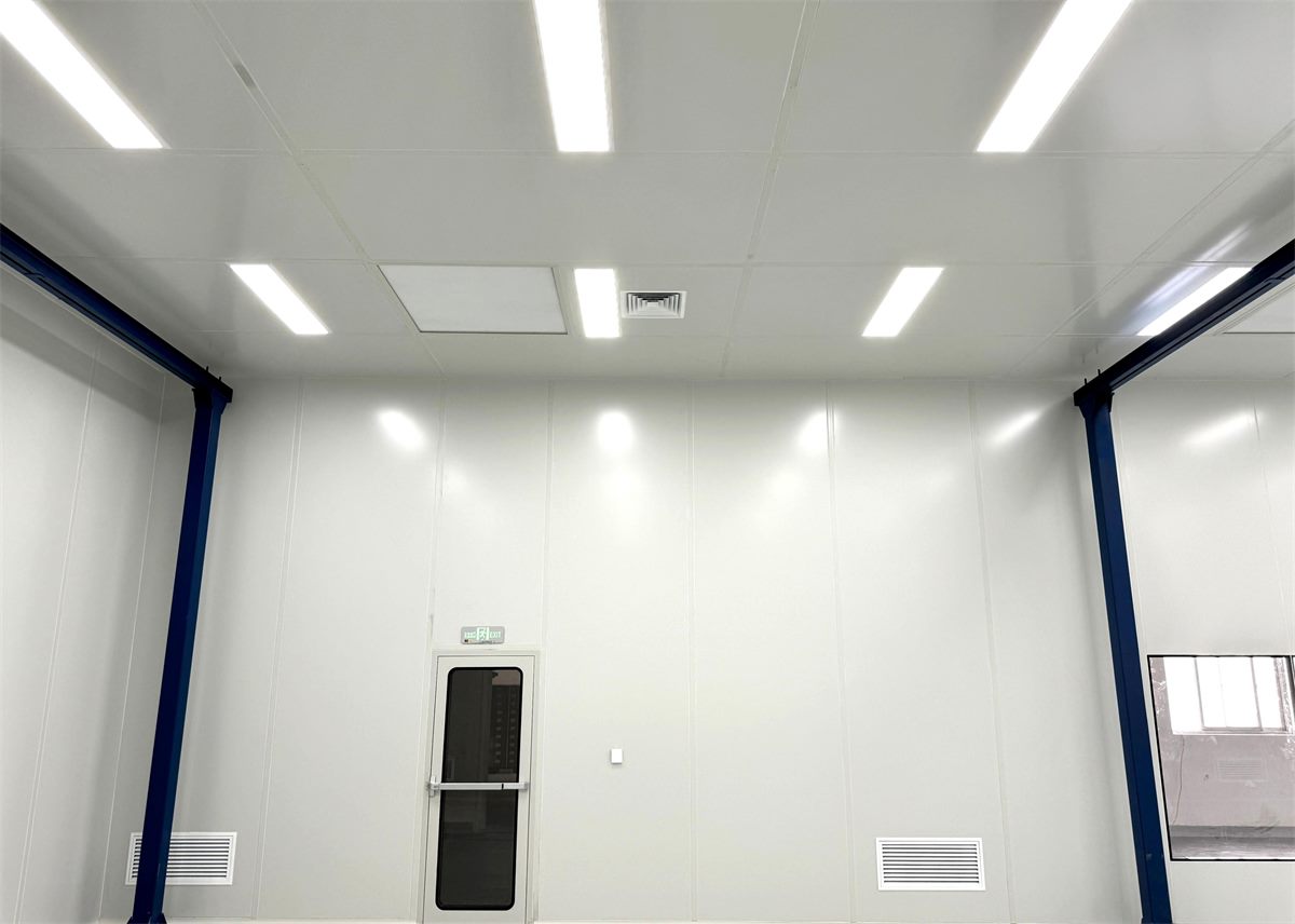 Bright pharmaceutical cleanroom interior with smooth white sandwich wall panels, flush ceiling lighting and an emergency exit door